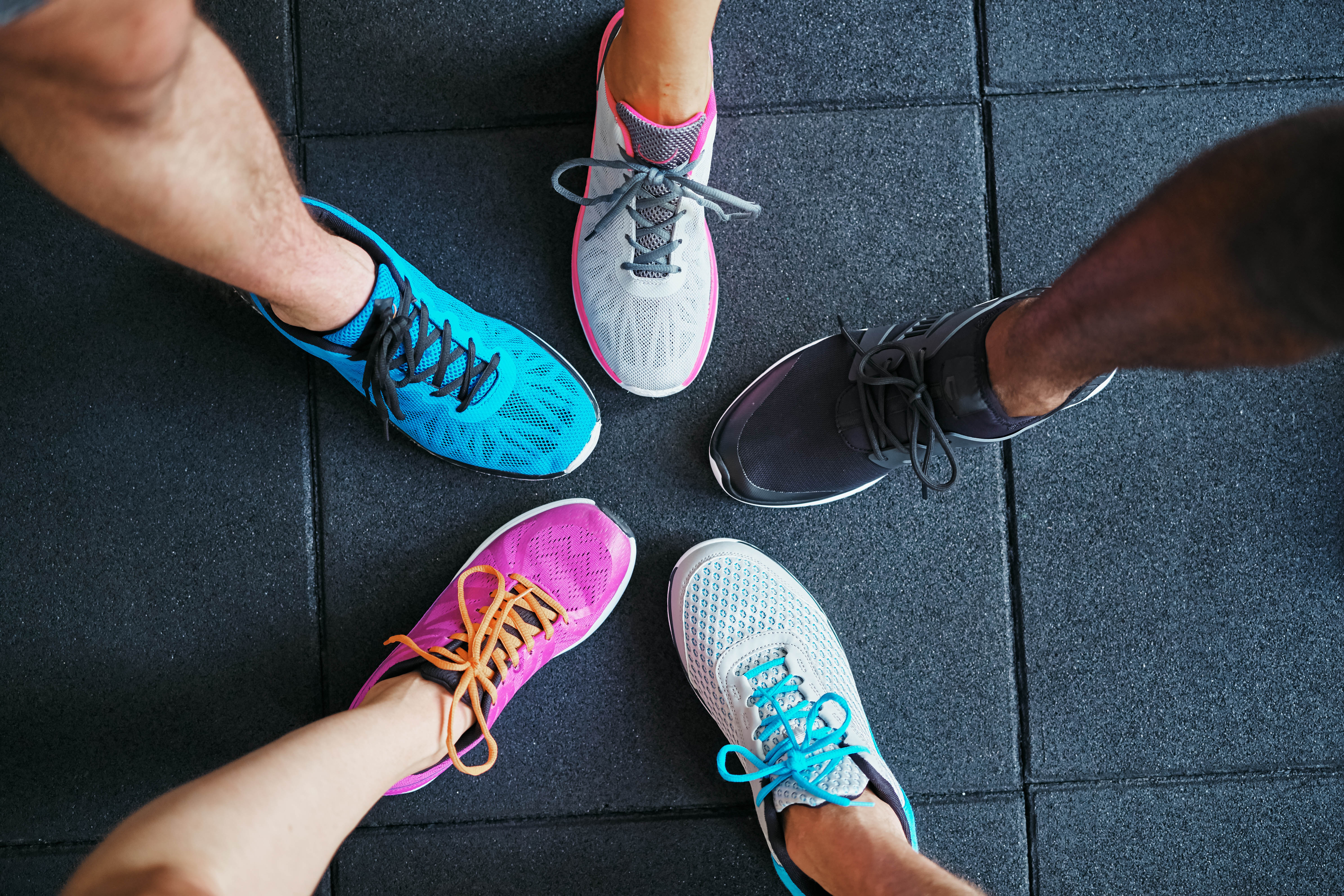 Five people wearing running shoes in the gym with their feet together in a circle